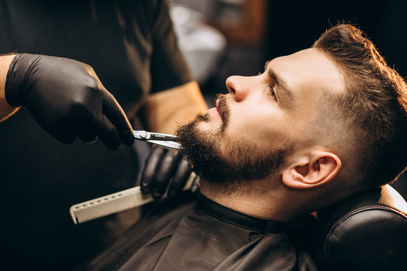 Client having a beard trim with scissors by a barber
